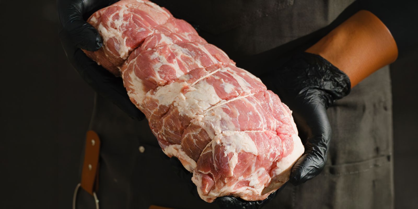 A butcher holding a rolled and tied heritage pork roast